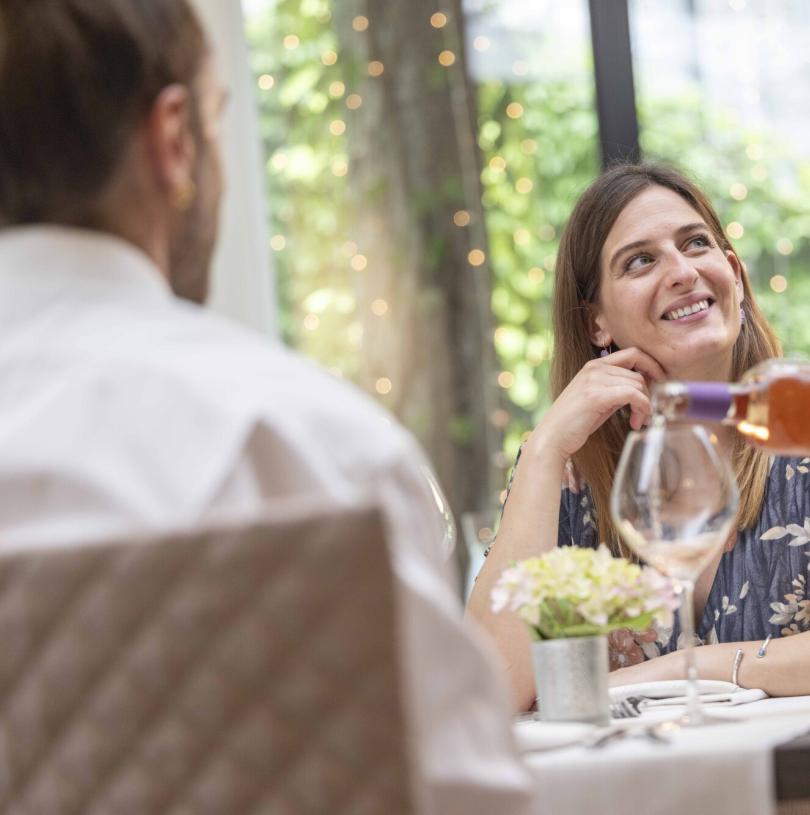 Donna sorridente a cena, vino versato, atmosfera calda e accogliente.